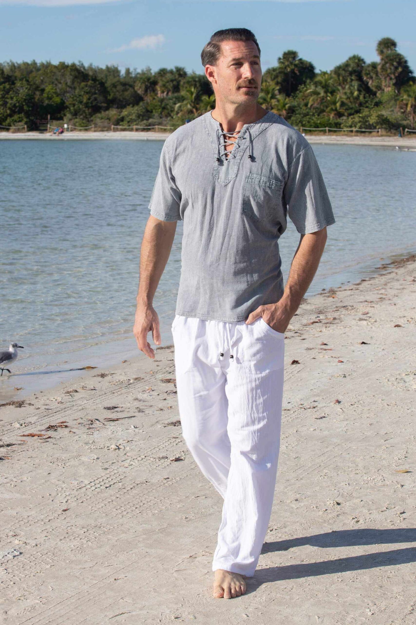 Man wearing Santorini pants on a beach, showcasing long gauze pants made from Peruvian Pima cotton with an elastic waistband and drawstrings.