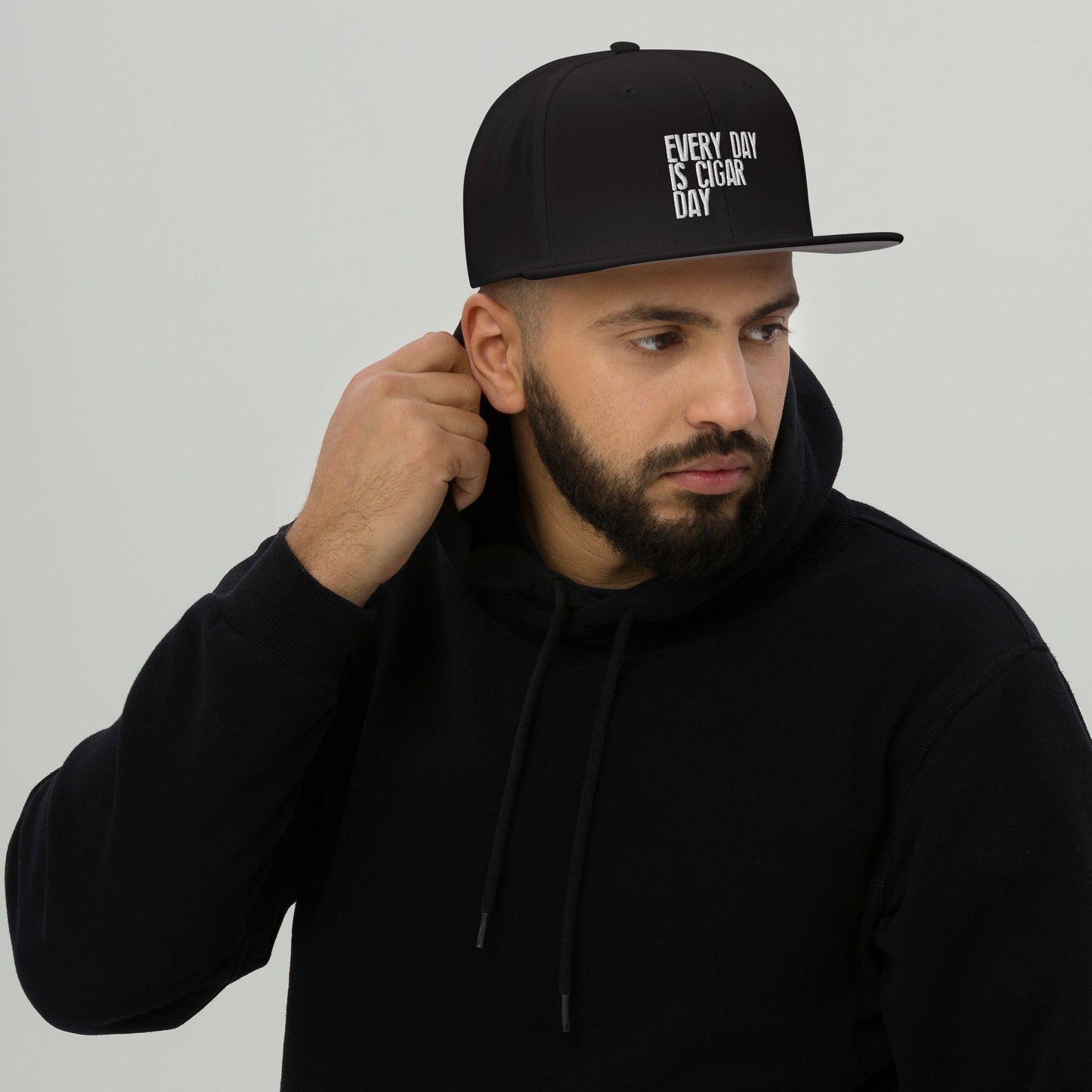 Black snapback hat with white text, worn by a model; structured high-profile design with flat visor.