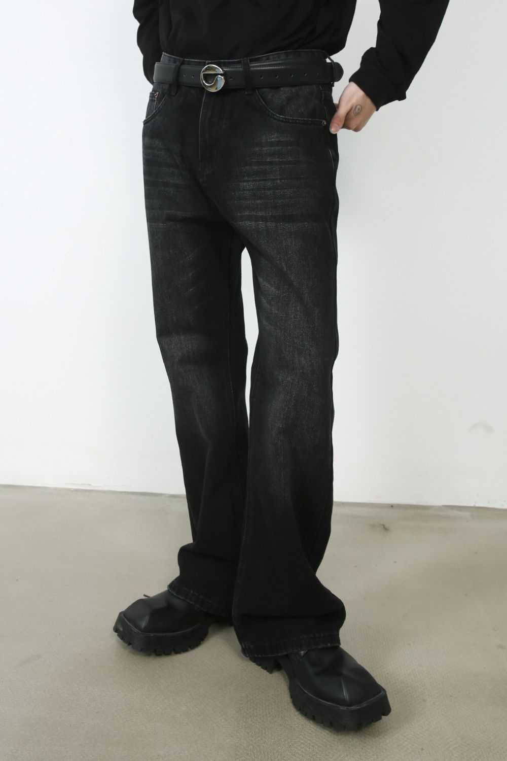 Men's mid rise jeans in black with no stretch, worn with a black belt and shoes.