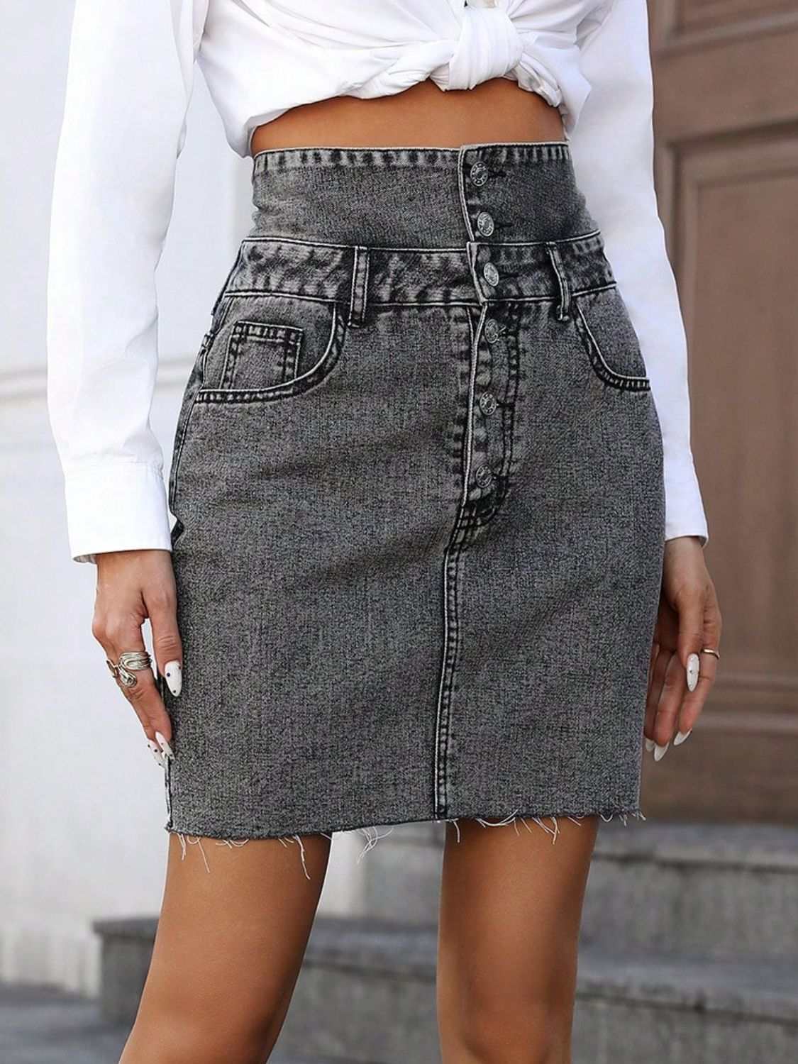 High-waist denim skirt with raw hem, buttoned front, and pockets.