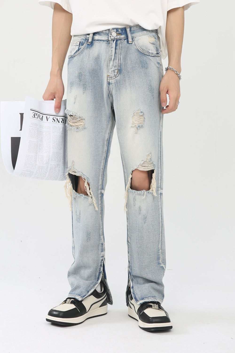 Men's distressed slit jeans with ripped design, holding newspaper.