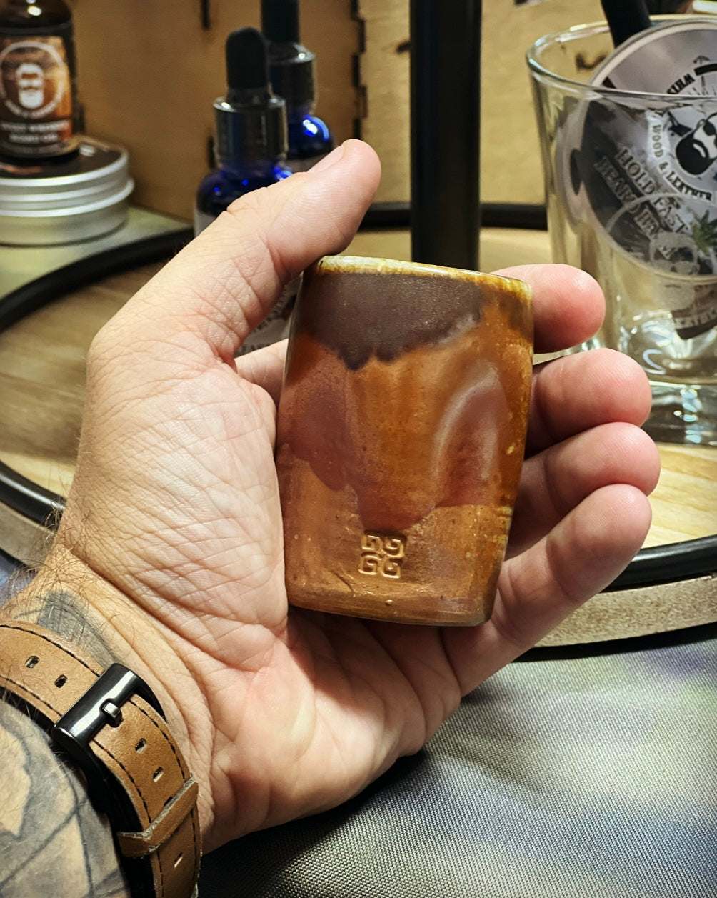 Hand holding a handcrafted brown pottery shot glass with unique design by Woodshop Pottery.