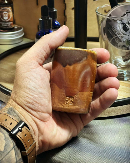 Hand holding a handcrafted brown pottery shot glass with unique design by Woodshop Pottery.