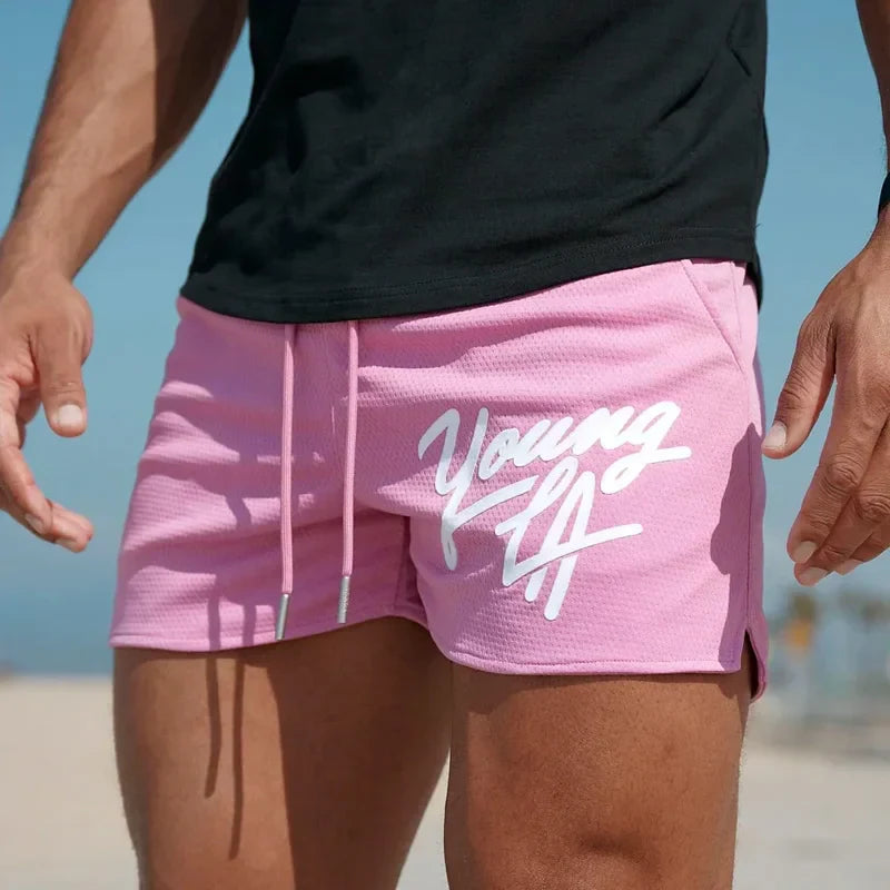 Young LA trendy beach shorts for men in pink with white logo, featuring elastic waist, perfect for summer sports activities.