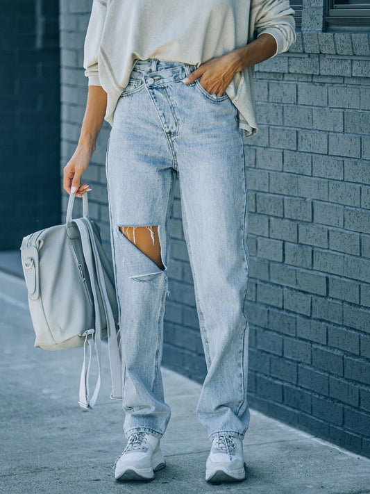 Distressed asymmetric waist jeans with ripped details and pockets.