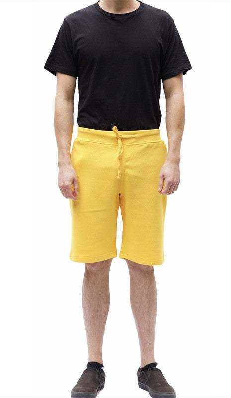 Yellow fleece sweat shorts with drawstring waistband, solid pattern, and side pockets, modeled by a person in black shirt and shoes. Made from cotton-polyester blend.
