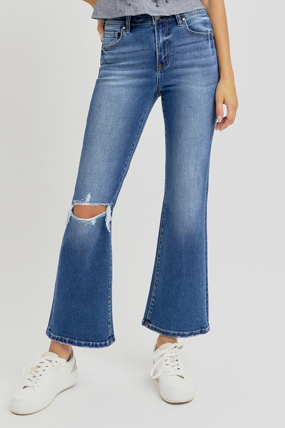 Distressed high rise crop flare jeans with ripped knee detail, styled with white sneakers.