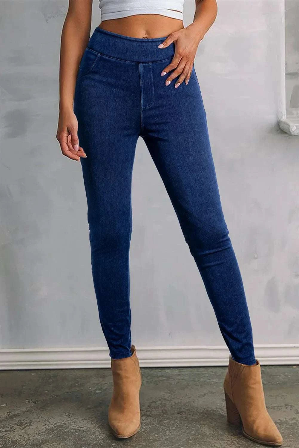 Woman wearing blue skinny jeans with pockets and tan ankle boots.