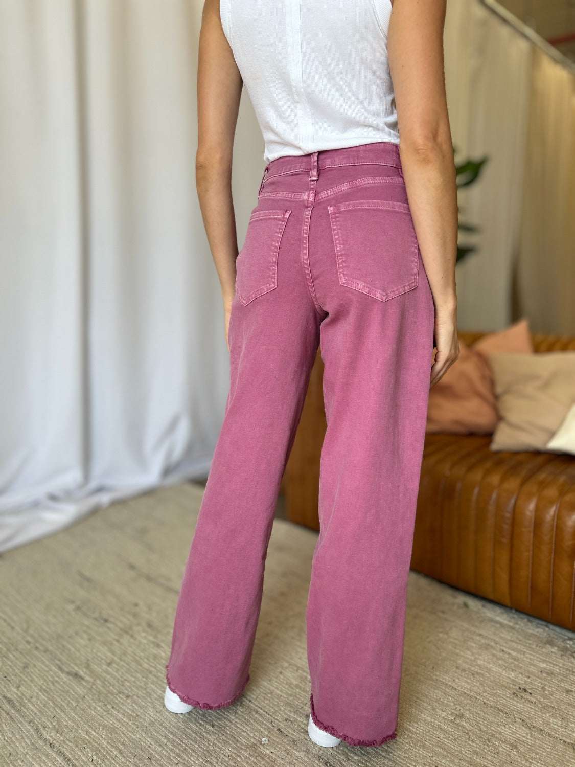Full size high rise wide leg jeans in pink, rear view showing pocketed design and raw hem.