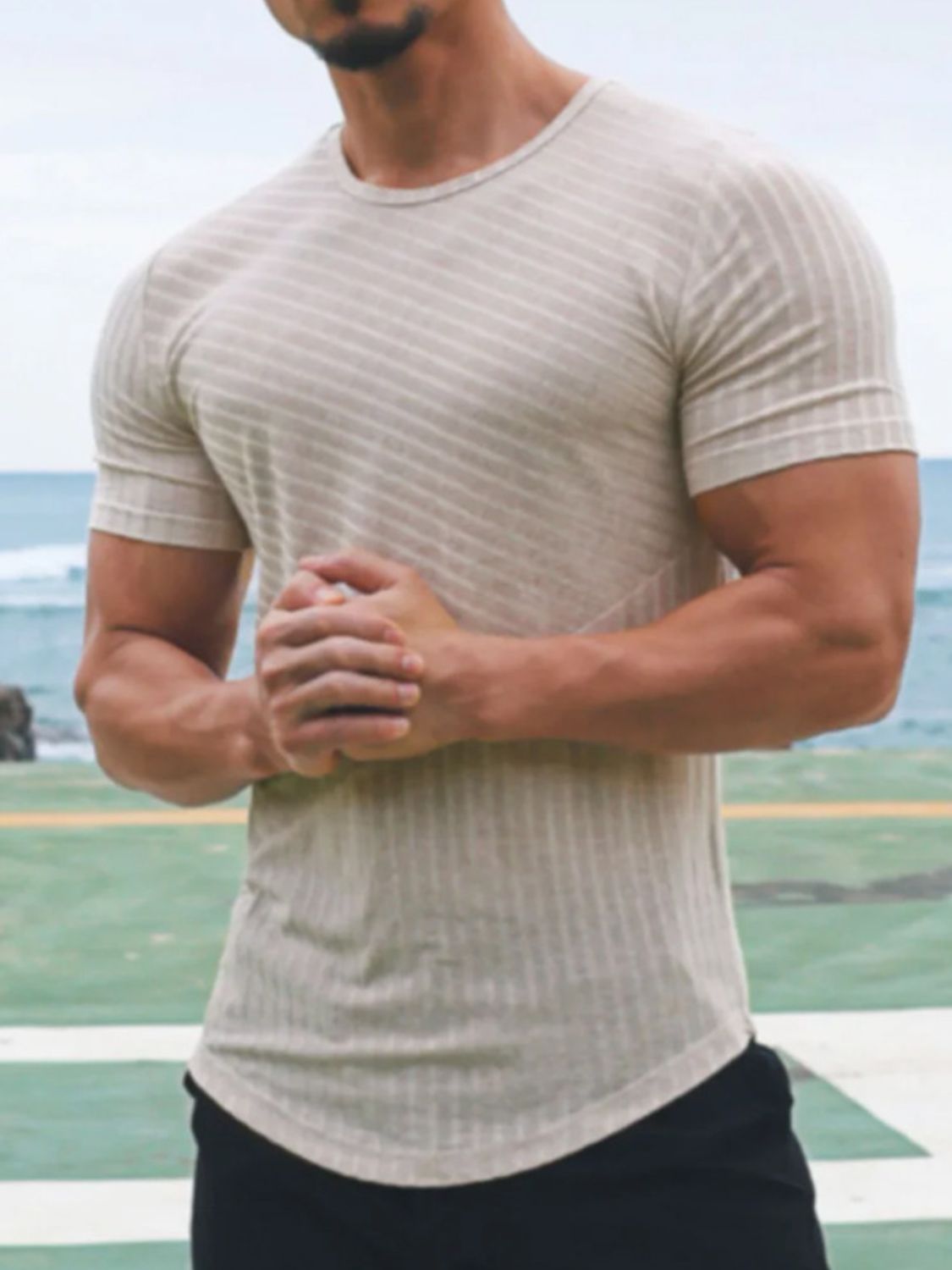 Men's round neck short sleeve striped t-shirt, beige, worn outdoors with ocean background.