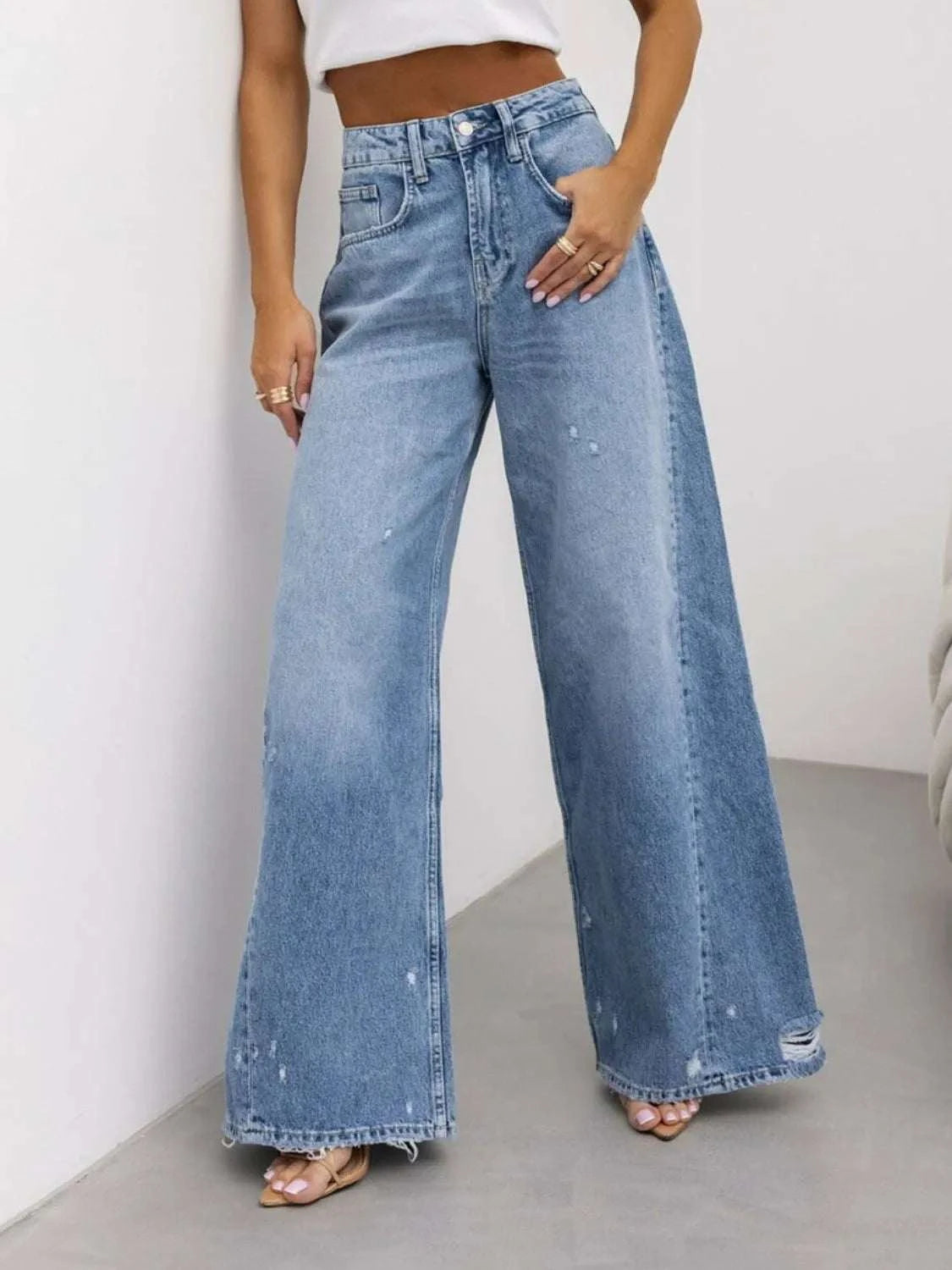 Distressed wide leg jeans with pockets and button details, made of cotton and polyester.