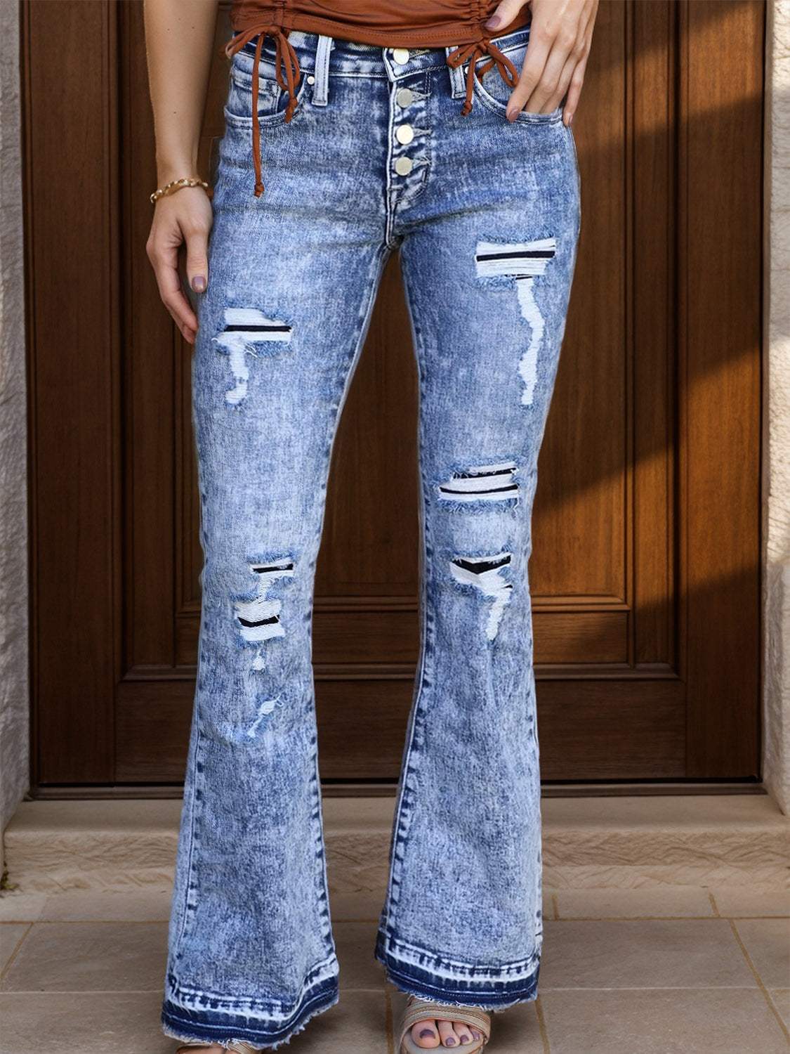 Distressed button-fly bootcut jeans with fringe and pockets.