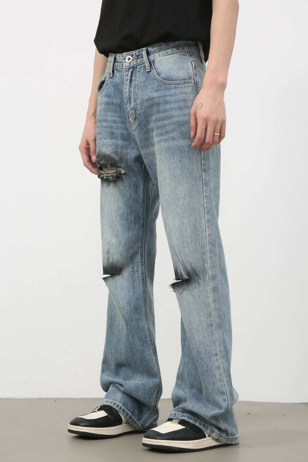 Men's distressed loose fit jeans with ripped details, no stretch, made of cotton, viscose, polyester, shown with casual sneakers.