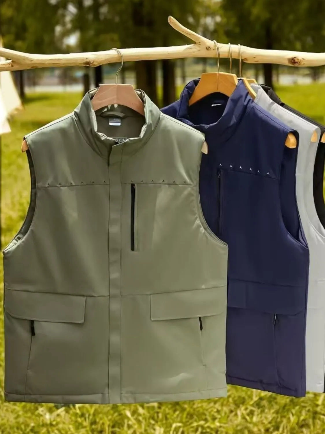 Men's full size zip up vests in multiple colors hanging on a wooden rack outdoors.